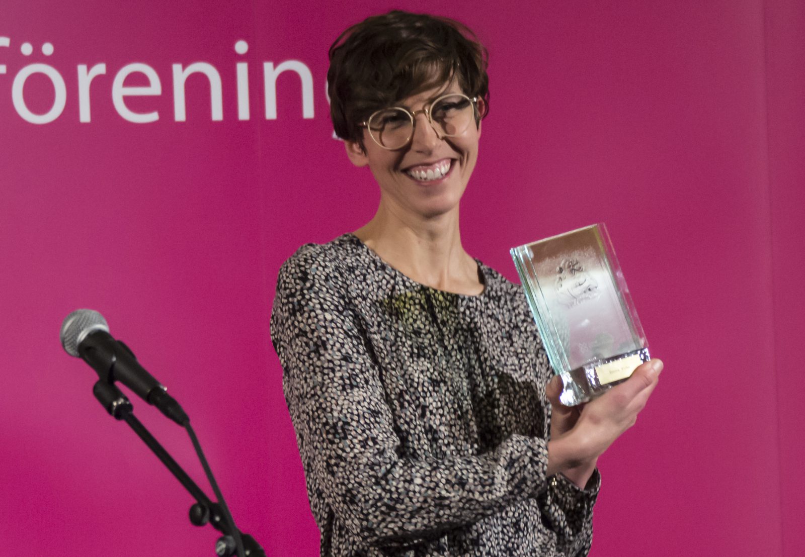 En glad kvinna håller upp en glasstatyett.