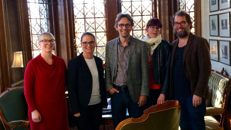Fem personer står i ett rum och tittar mot kameran.