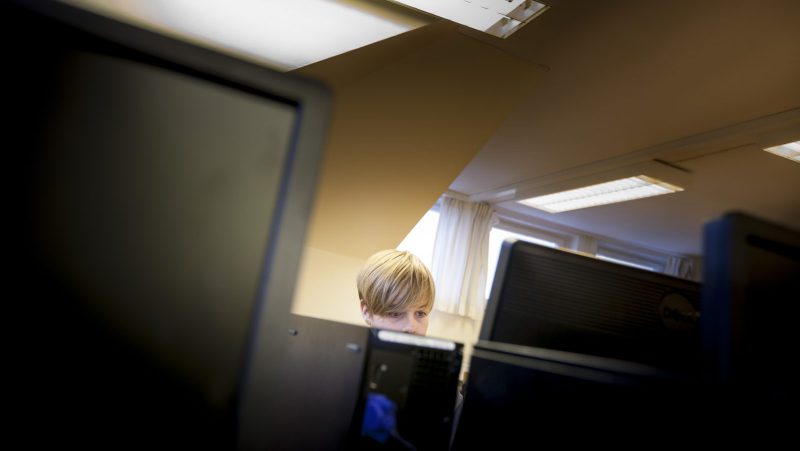 Ett barns huvud sticker delvis fram bakom flera datorskärmar.