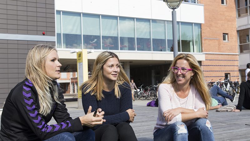 Tre kvinnor sitter framför en större byggnad.