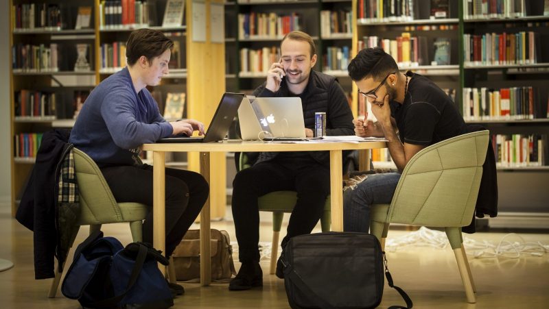 Tre studenter sitter vid bord i universitetsbibliotek